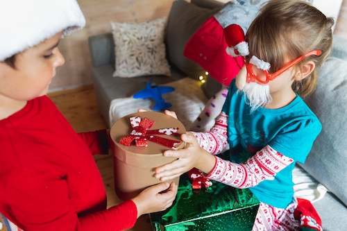 two kids exchanging gifts for christmas - image featured in article image feature a baby with christmas clothing and is featured in article Dressing your baby in style this Christmas 